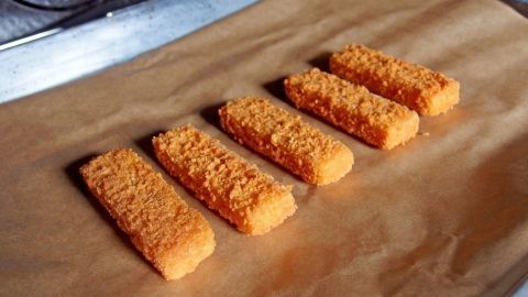 Fischstäbchen zubereiten, ohne den Herd putzen zu müssen. Fischstäbchen liegen auf einem Backblech mit Backpapier, bereit zum Braten ohne Herd putzen, in einer gut beleuchteten Küche.