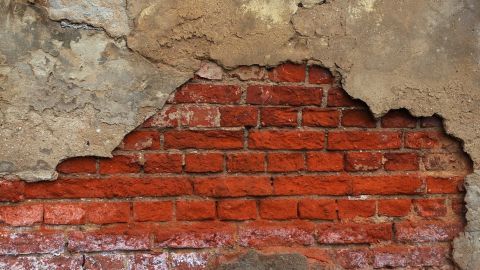Ein beschädigter Mauerwerksbereich zeigt freiliegende Ziegelsteine, umgeben von bröckelndem Putz und Salpeterablagerungen.