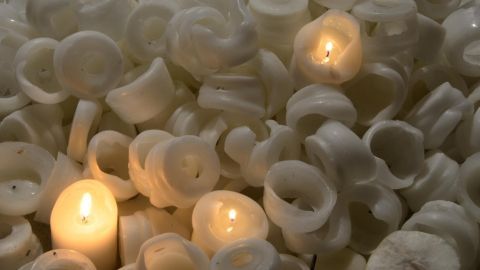 Kerzenreste leuchten in dunkler Umgebung, umgeben von weiteren weißen Wachsresten. Drei Flammen brennen sanft.