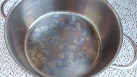 Ein Edelstahltopf mit verfärbtem Boden steht auf einem hellen Untergrund und zeigt Rückstände und Flecken im Inneren.