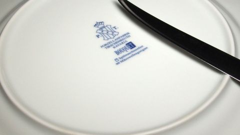 Ein schwarzes Messer liegt auf einem wei&szlig;en Teller, der das Markenzeichen eines Porzellanherstellers zeigt.