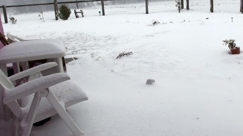 Ein Stuhl liegt im Schnee, während weitere Schneemassen den Garten bedecken und Landschaft verdecken.