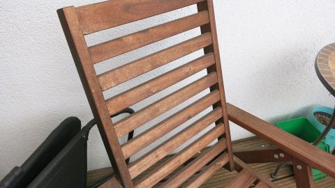 Ein Holzstuhl steht auf einer Terrasse, während er für die Lagerung im Freien bereit ist, um Witterungseinflüssen zu trotzen.