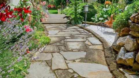 Ein gepflasterter Gartenweg schlängelt sich durch eine blühende Landschaft voller bunter Blumen und Pflanzen.