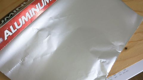 Mit langen, an Bambusstäbe gebundene Alufolie-Stücke, hält man Vögel fern von dem, was sie nicht fressen sollen! Eine faltige Alufolie liegt auf einem Holzuntergrund, bereit zur Herstellung von kreativen Vogelscheuchen im Garten.