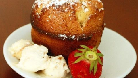 Ein Caramac-Küchlein mit Puderzucker, serviert neben cremigem Eis und einer frischen Erdbeere auf einem weißen Teller.