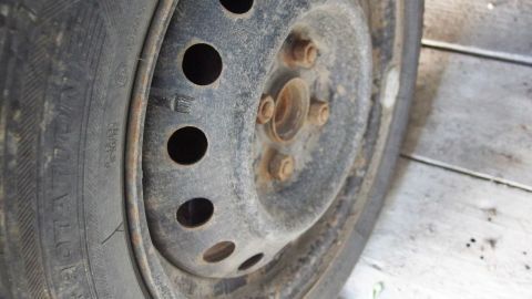 Ein schmutziger Reifen mit einem alten, rostigen Rad und mehreren Bohrungen ist auf einem staubigen Untergrund abgebildet.