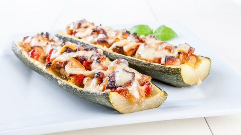 Zucchinihälften sind mit geschmolzenem Käse, Thunfisch und Gemüse gefüllt und auf einem weißen Teller angerichtet.