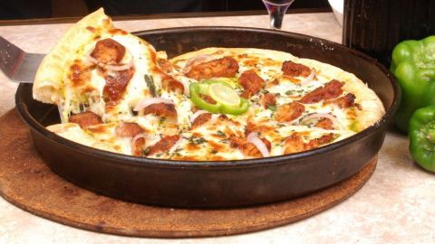 Eine frisch gebratene Tiefgefrorene Pizza wird aus einer Pfanne auf einen Teller gehoben und von grünen Paprika umgeben.