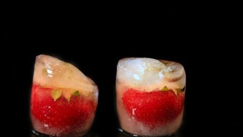 Runde Erdbeereiswürfel sind sichtbar, gefroren mit frischen Erdbeeren innerhalb, auf schwarzem Hintergrund.
