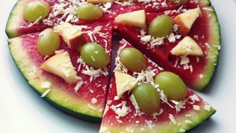 Melonen-Pizza: Wassermelonenscheiben belegt mit Weintrauben und Apfelstücken auf einem Teller, wie eine süße Pizza angerichtet.