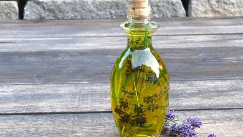 Ein Glasfläschchen mit Lavendelöl steht auf einem Holztisch, umgeben von einigen frischen Lavendelblüten.