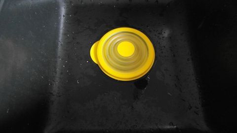 In diesem Bild siehst du den Ablauf deines Waschbeckens mit einem praktischen Abflussstopfen. Er ist ein hilfreiches Werkzeug, um Verstopfungen ohne Chemie zu beseitigen. Weitere Tipps findest du im Artikel. Ein gelber Stöpsel liegt in einem dunklen Spülbecken, während Wasser still steht, was auf einen verstopften Abfluss hinweist.