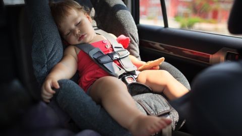 Ein Kleinkind schläft in einem Kindersitz im Auto, was auf die potenzielle Lebensgefahr durch Hitzeentwicklung hinweist.