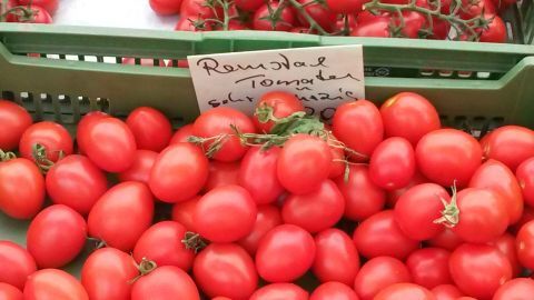 Runde, rote Tomaten liegen in einem Korb. Ein handgeschriebene Schild beschreibt sie als "Runde Tomaten".
