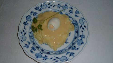 Ein Teller mit Senfsauce zeigt eine cremige, gelbe Sauce, garniert mit einem Ei, auf einem blauen, floral dekorierten Geschirr.