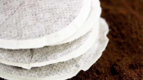 Kaffeepads liegen übereinander auf gemahlenem Kaffee, bereit zur Verwendung für eine frisch gebrühte Tasse.