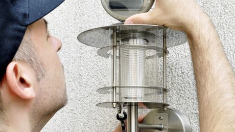 Ein Handwerker befestigt eine moderne Solarleuchte an einer Wand, um den Außenbereich zu beleuchten und zu pflegen.