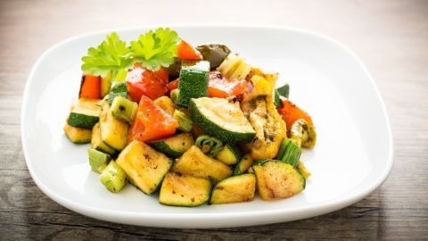 Bunte Grillgemüse-Salat-Mischung auf einem weißen Teller, frisch zubereitet und dekoriert mit einem Blatt Petersilie.