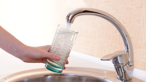 Ein Hand hebt ein Glas unter einen Wasserhahn, der frisches Trinkwasser fließen lässt, in einer modernen Küche.