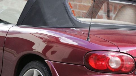 Ein roter Cabrio mit einem schwarzen Stoffdach steht an einer Backsteinmauer, die Heckscheibe ist leicht trüb.