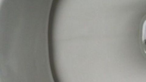 Eine glatte, weiße Keramikoberfläche zeigt einen klaren Wasserstrom, während Urinstein und Kalk entfernt werden.