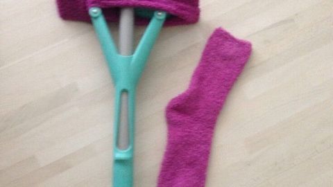 Ein Wischmopp mit einer pinken Socke daneben auf einem hellen Laminatboden, bereit zum Putzen mit Kuschelsocken.