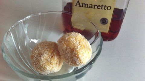 Zwei runde Schneebälle mit Amaretto liegen in einer Glas-Schüssel, umgeben von einer Flasche Amaretto in einem hellen Raum.