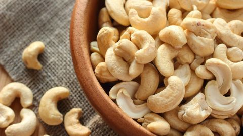 Geröstete Cashewkerne sind in einer Schüssel angeordnet, während einige auf einer rustikalen Tischdecke liegen.