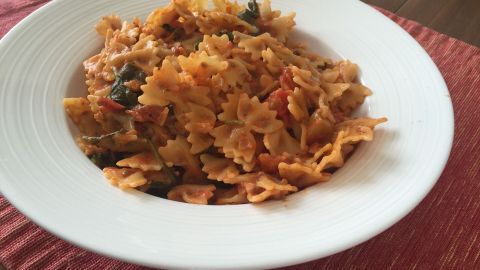 Eine Schüssel mit farbenfrohen, veganen Nudeln in Tomatensoße steht auf einem Tisch mit einer roten Tischdecke.