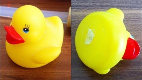 Eine gelbe Gummiente liegt auf einem Holzuntergrund, mit geöffnetem Verschluss an der Unterseite zum Befüllen mit Wasser.