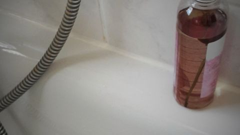 Eine Flasche Badeöl steht neben einer Badewanne, während das Wasser in der Wanne trocknet und Reste hinterlässt.