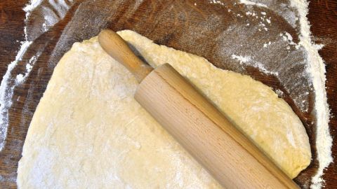 Ein ausgerollter Pizzateig liegt auf einer bemehlten Fläche, während ein Nudelholz darauf platziert ist, bereit für den nächsten Schritt.