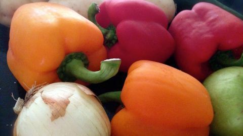 Bunte Paprika und Zwiebeln liegen in einer Schüssel, bereit zum Putzen ohne Dreck auf der Arbeitsplatte.
