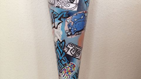 Eine bunte Schultüte im Graffiti-Look steht auf einem Holzfußboden, dekoriert mit stilisierten Zeichnungen und Farben.