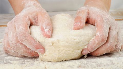 Zwei Hände kneten einen weichen Teig auf einer mit Mehl bestäubten Arbeitsfläche, bereit zur weiteren Verarbeitung für Quarkölteig.