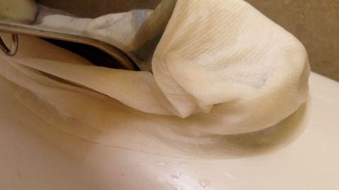 Ein nasses Küchenpapier liegt auf einer Armatur, während es Kalk entfernt. Die Umgebung ist eine Küchenoberfläche.