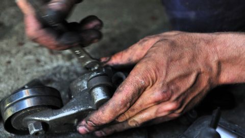 Ölige Hände halten ein Metallteil, während eine Person mit einem Werkzeug daran arbeitet, um es zu reinigen.