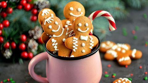 Lebkuchenfiguren stehen fröhlich in einer rosa Tasse, umgeben von festlichem Dekor und einem Zuckerstangenakzent.
