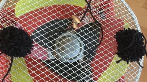 Ein Ventilator mit bunten Blättern und schwarzen Pompons bläst frische Luft in einem gemütlichen Raum.