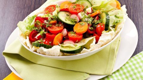 Ein bunter Salat mit frischen Zutaten und gerösteter Paprika wird in einer zweifarbigen Schüssel serviert, umgeben von einem hellen Tuch.