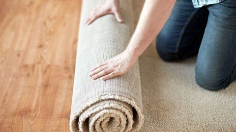 Ein Mensch kneelt auf einem Laminatboden und rollt einen Teppich aus, um Klebebandreste zu entfernen.