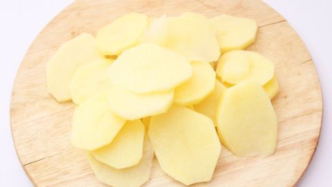 Kartoffelscheiben liegen roh und ungekocht auf einem hölzernen Schneidebrett, bereit für weitere Zubereitungsschritte.