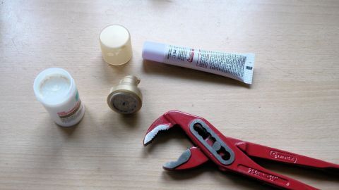 Ein Kosmetikspender liegt auf einem Tisch, während er mit einem roten Werkzeug und verschiedenen Cremetuben aufgefüllt wird.