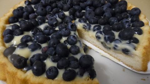 Ein Obstkuchen mit einer Oberfläche aus vielen Heidelbeeren liegt auf einem Teller, ein Stück wurde entnommen.