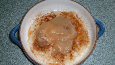 Ein Schälchen Milchreis steht auf einer Arbeitsplatte, bedeckt mit Apfelmus und Zimt, traditionell nach Oma-Methode zubereitet.