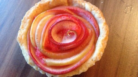 Eine Apfel-Rosen-Tarte liegt auf einem Holztisch. Die Apfelscheiben sind kunstvoll in Form einer Rose angeordnet.