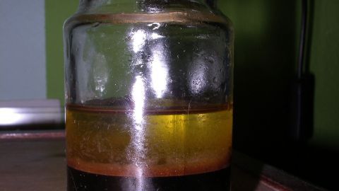 Ein Glasbehälter mit Schichten aus Essig und Öl steht auf einem Tisch vor einer grünen Wand, bereit für die Möbelpflege.