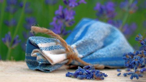 Ein Duftsäckchen aus blauer und weißer Stoffbindung liegt auf einer Fläche, umgeben von blühendem Lavendel.