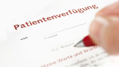 Ein Dokument mit dem Titel "Patientenverfügung" wird von einer Hand mit einem roten Stift unterschrieben, um wichtige Wünsche festzuhalten.